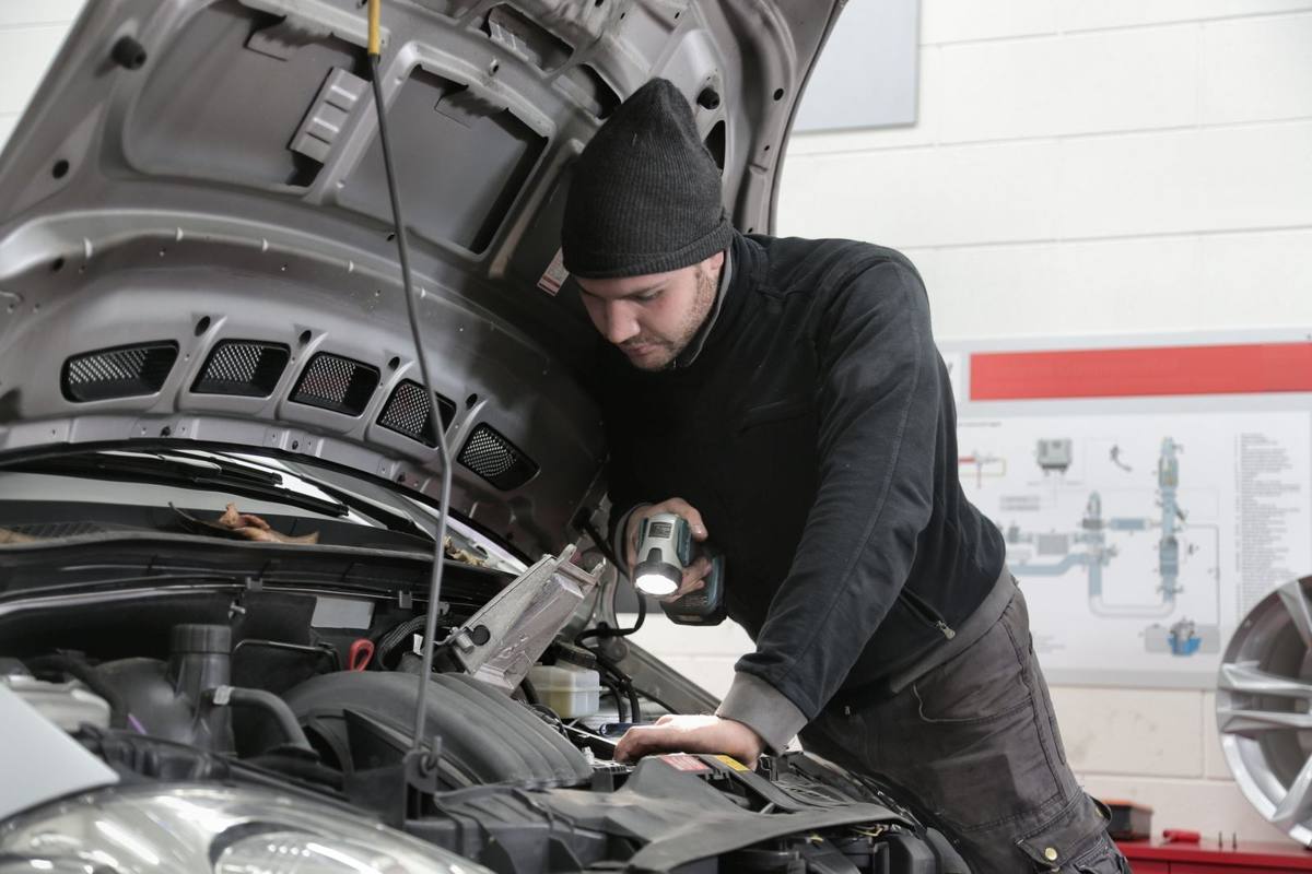 A mechanic shining a flashlight into an engine bay during an inspection